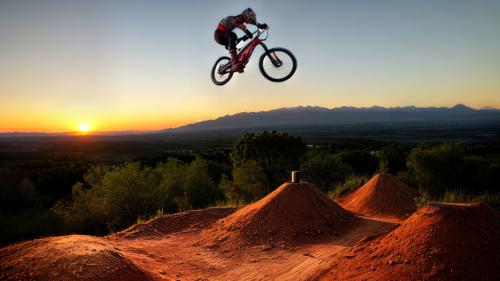 mountain bike stunting on dirt jumps in the sunset